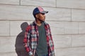 Stylish african man wearing red plaid shirt, baseball cap, looking away, young guy posing on city street, gray brick wall Royalty Free Stock Photo