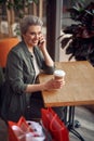 Stylish aged woman talking by phone in cafe