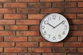 Stylish analog clock hanging on brick wall