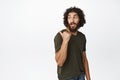 Stylish arab guy with long beard, pointing behind his shoulder, looking at advertisement, sale promo, standing over