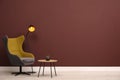 Stylish armchair, table and lamp near brown wall, space for text