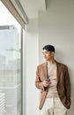 Young Asian business man holding phone looking at window standing in office. Royalty Free Stock Photo