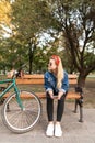 Stylish attractive girl sitting on a bench in a park near a bicycle with a smartphone in his hands, and looking away Royalty Free Stock Photo