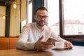 Stylish attractive pleasant fellow young businessman from Europe in glasses, with a beard and a white shirt sits at a table in a