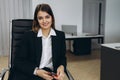 Stylish attractive young businesswoman with a lovely smile sitting in front of a table in the office grinning at the camera