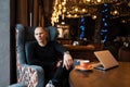 Stylish attractive young man in a fashionable shirt in stylish black jeans in sneakers sits on an easy chair in a restaurant on a Royalty Free Stock Photo