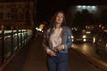Stylish attractive young woman in denim jacket, evening city background.Portrait of girl student walking on night street Royalty Free Stock Photo