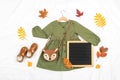 Stylish autumn set of child clothes. Green dress, brown bag, shoes, letter board frame and autumn leaves on white background.