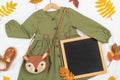 Stylish autumn set of child clothes. Green dress, brown bag, shoes, letter board frame and autumn leaves on white background.