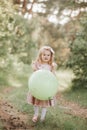 Stylish baby girl holding big balloon wearing trendy pink dress in meadow. Playful. Birthday party Royalty Free Stock Photo