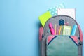 Stylish backpack with different school stationery on light blue background, top view. Space for text