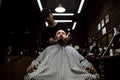 The stylish barbershop. The fashion barber tidies up beard of brutal man sitting in the armchair