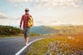 Stylish barefoot bearded male hitchhiker traveler in a hat and with a backpack walks along a country road in the