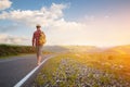 Stylish barefoot bearded male hitchhiker traveler in a hat and with a backpack walks along a country road in the