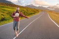 Stylish barefoot bearded male hitchhiker traveler in a hat and with a backpack walks along a suburban asphalt road in