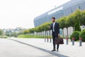 Stylish bearded business man with travel bag and mobile phone in hands walks on city street modern urban background. Businessman Royalty Free Stock Photo