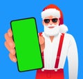 Stylish bearded Santa Claus in sunglasses stands with a smartphone in his hand. Close-up of the green screen of the phone. Place