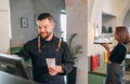 Stylish bearded smiling waiter dressed black uniform using point of sale order terminal system touch Screen and waitress woman