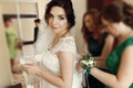 Stylish beautiful bridesmaids helping gorgeous brunette bride in white dress get ready for wedding, morning preparations, woman Royalty Free Stock Photo