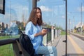 Beautiful girl waits for subway or tram on public transport station in the morning. Happy young woman with cup of coffee