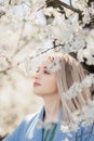 Stylish beautiful woman sensually posing among blooming apple branches in sunny spring, calm moment. Portrait of happy young