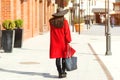 Stylish beautiful woman walking in street. Girl wearing red coat, black hat and holding trendy bag. Fashion outfit, autumn trend, Royalty Free Stock Photo