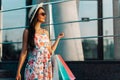 Young woman, in hat and summer clothes, enjoys shopping while holding shopping bags, in a shop window in the city Royalty Free Stock Photo