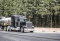 Stylish black big rig semi truck with cylindrical tank semi trailer for liquid transportation running on the highway road with Royalty Free Stock Photo