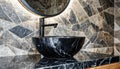 Stylish black marble round vessel sink and wall mounted faucet on stone wall. Interior design of modern bathroom Royalty Free Stock Photo