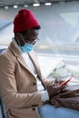 Stylish Black traveler man using phone, wearing mandatory face mask to protect yourself from contact with flu virus, pandemic ÃÂ¡