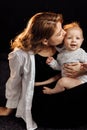 Stylish blond haired young mother gently sitting and holding baby girl. Attractive woman smiling and hugging her little Royalty Free Stock Photo