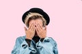 Stylish blond woman closes eyes with her hands in jeans jacket and hat on pink background Royalty Free Stock Photo