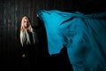 Stylish blonde on a dark background with bright flying fabric, color blue