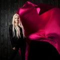 Stylish blonde on a dark background with bright flying fabric, color pink