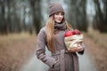 Stylish blonde woman in trendy urban outwear posing cold weather forest park alley with package of red apples. Fall mood concept. Royalty Free Stock Photo