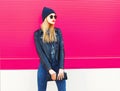 Stylish blonde woman model in profile looking away wearing rock black style jacket, hat, with handbag clutch on city street Royalty Free Stock Photo