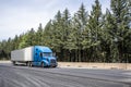 Stylish blue big rig long haul industrial semi truck transporting cargo in dry van semi trailer running on the highway road with Royalty Free Stock Photo