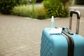 Stylish blue suitcase with protective mask and antiseptic spray outdoors, space for text. Travelling during coronavirus pandemic