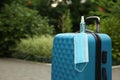 Stylish blue suitcase with protective mask and antiseptic spray outdoors, space for text. Travelling during coronavirus pandemic