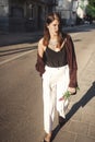 Stylish bohemian girl with modern jewelry walking in sunny street. Happy hipster carefree girl in boho look with flowers relaxing