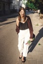 Stylish bohemian girl with modern jewelry walking in sunny street. Happy hipster carefree girl in boho look with flowers relaxing