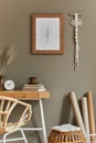 Stylish bohemian interior of home office space with wooden desk, rattan armchair, brown mock up poster frame, macrame, office.