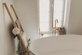 Stylish boho bathroom design. Modern bathtub with golden faucet from floor, wooden ladder with towels and big window, modern eco Royalty Free Stock Photo