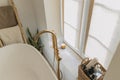 Stylish boho bathroom design. Modern bathtub with golden faucet from floor, wooden ladder with towels and big window, modern eco Royalty Free Stock Photo