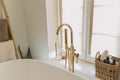 Stylish boho bathroom design. Modern bathtub with golden faucet from floor, wooden ladder with towels, washing essentials and big Royalty Free Stock Photo