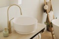 Stylish boho bathroom design. Modern ceramic sink with golden faucet on rustic stand with soap and towel on background of bathtub Royalty Free Stock Photo