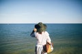 Stylish boho girl in hat looking at sea in sunny evening light from sandy cliff, back view. Happy young hipster woman relaxing on Royalty Free Stock Photo