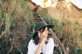 Stylish boho girl in hat sitting on wooden stairs in sunny light at sandy cliff near sea. Happy young fashionable woman relaxing Royalty Free Stock Photo