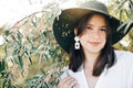 Stylish boho girl with modern earrings posing among green olive branches in soft evening light. Happy young fashionable woman Royalty Free Stock Photo