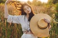 Stylish boho woman with straw hat posing among wildflowers in sunset light. Summer delight and travel. Young carefree female in Royalty Free Stock Photo